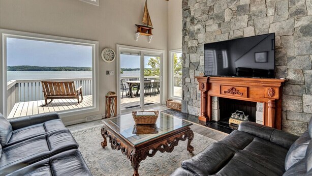A spacious living room with a stone fireplace, leather sofas, a glass coffee table, and a TV mounted on the wall.