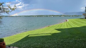 A lakeside view with a rainbow, a grassy lawn, and a building in the background.