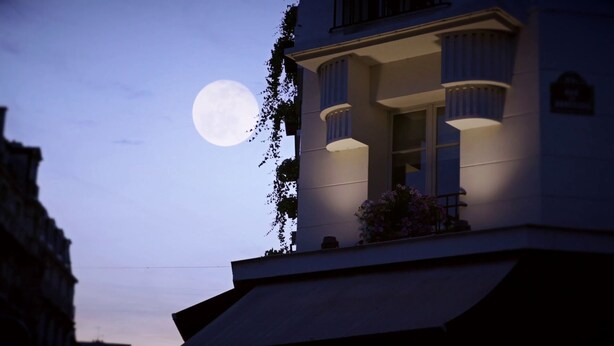 A building with a balcony overlooking a body of water, with a full moon visible in the sky.