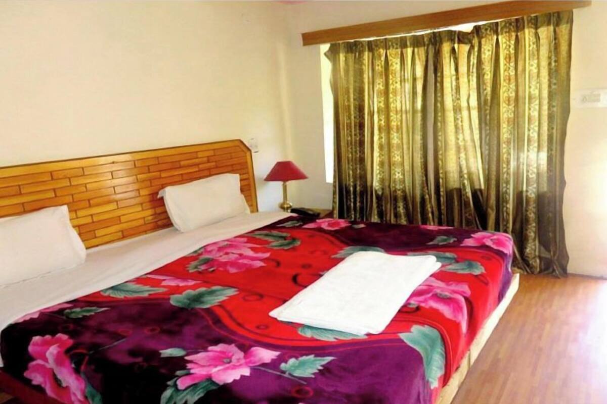A bed with a floral bedspread, a wooden headboard, and a red lamp beside it.