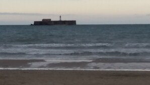 Uma praia com um farol ao longe.