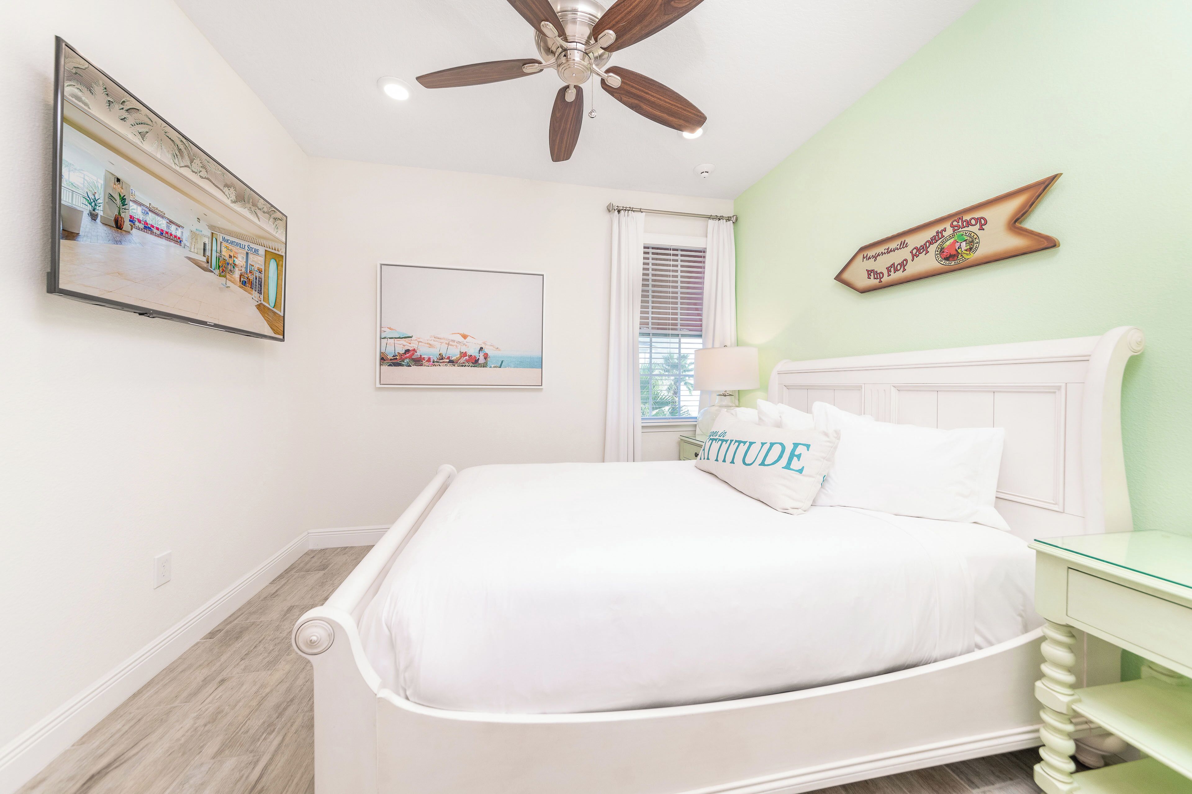 A bedroom with a bed, a ceiling fan, a wall-mounted sign, and a window with blinds.