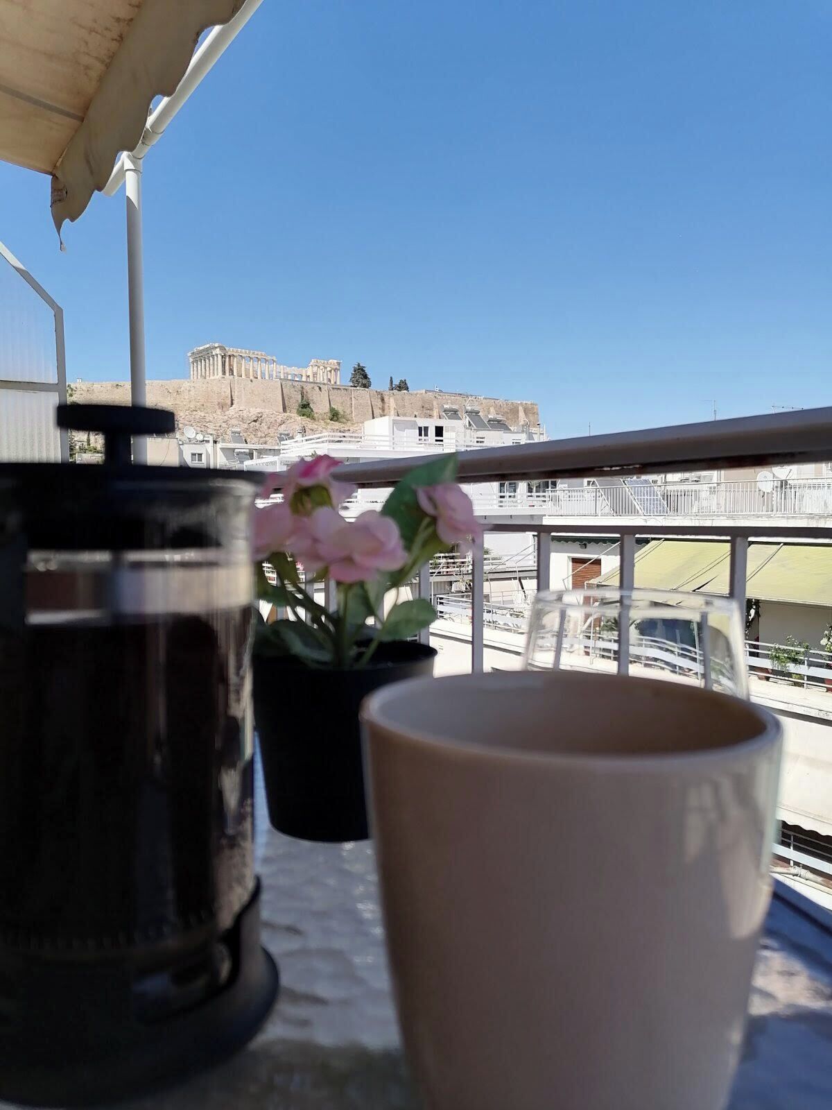 Un balcon donnant sur un bâtiment historique, une plante en pot et une machine à café.