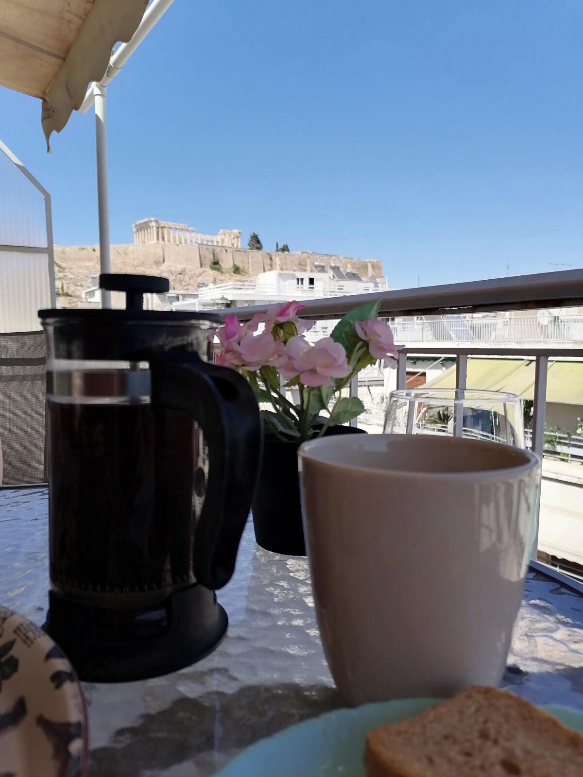 A balcony with a coffee maker, a mug, and a plate with bread. In the background, there is a view of a historic building.