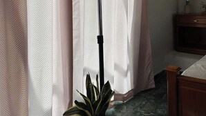 A room with a bed, a nightstand, a lamp, a potted plant, and a window with curtains. - Acropolis View Charming Loft (Athens)
