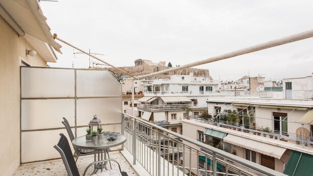 A balcony with a table and chairs, overlooking a cityscape with buildings and a distant view of a historical site. - Acropolis View Charming Loft (Athens)