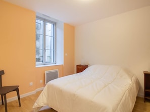 Quarto com cama, cadeira, janela e radiador.