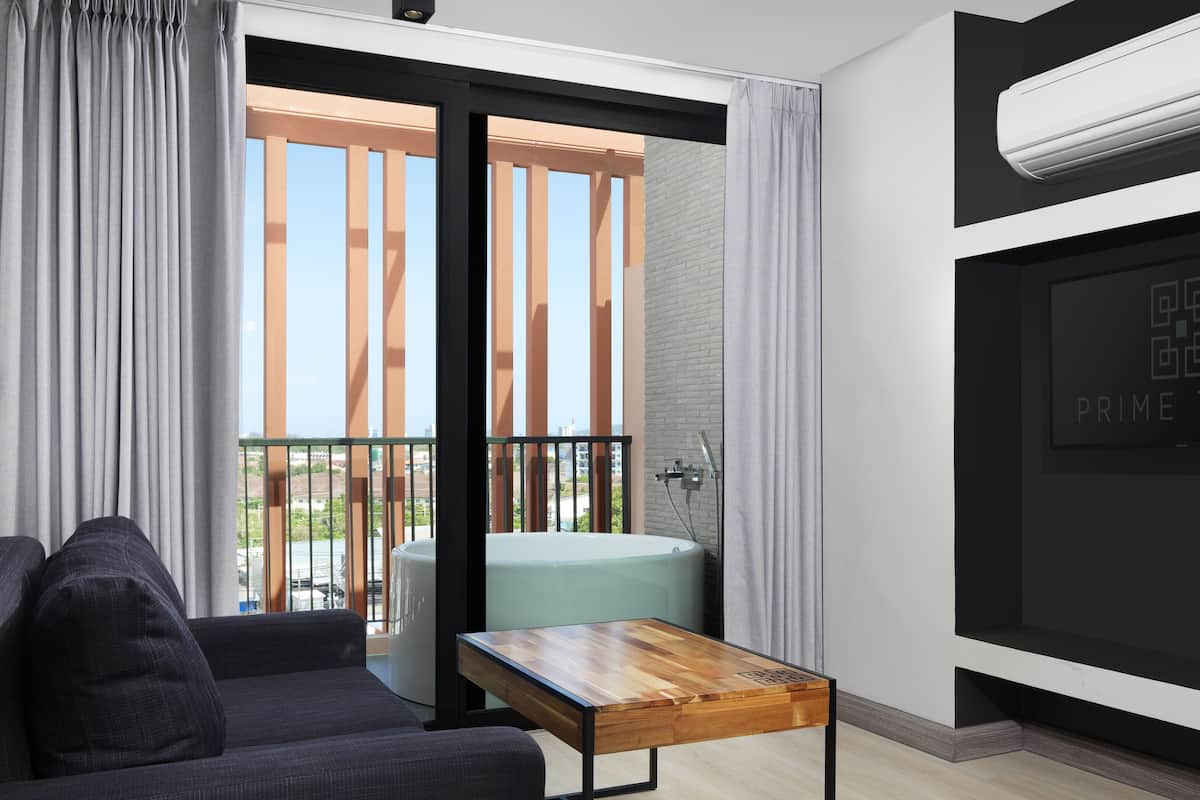 A modern hotel room with a balcony, a seating area, and a built-in air conditioning unit.