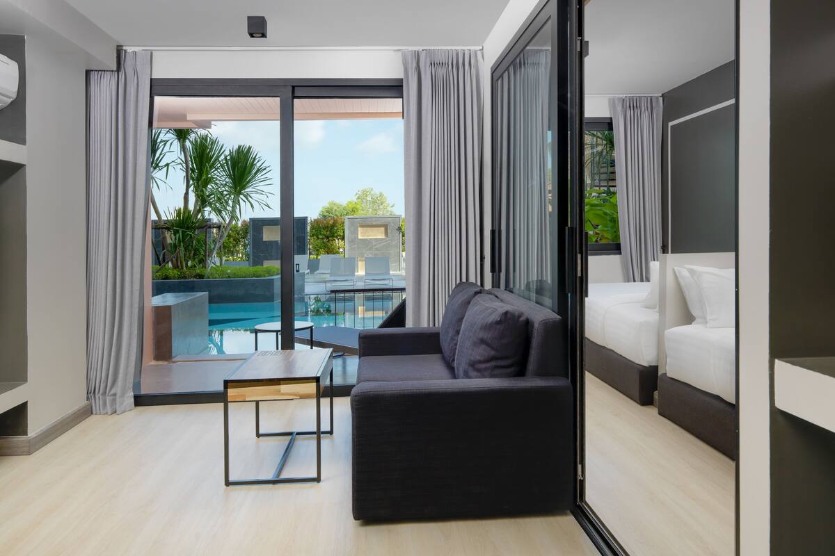 A modern living room with a sofa, a small table, and a view of a swimming pool and greenery outside.