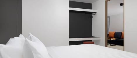 Et moderne hotelværelse med en seng, en rød skammel, en sort hylde og et spejl, der afspejler en sofa og et bord.