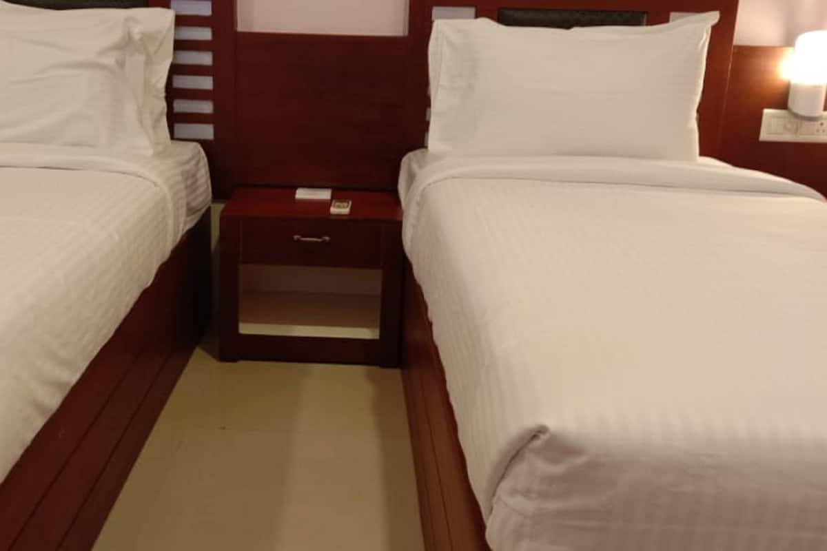 A hotel room with two single beds, a wooden headboard, a nightstand, and a wall-mounted light.