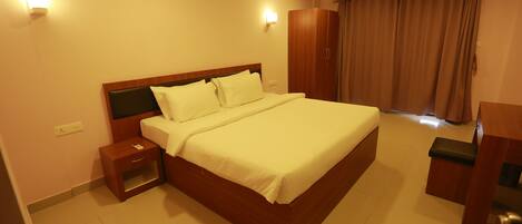 A hotel room with a large bed, a nightstand, a wardrobe, and a desk.