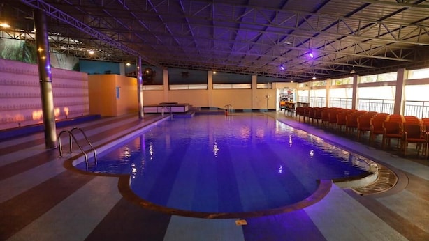 Una piscina interior con superficie de agua cristalina, rodeada de suelo y paredes con azulejos, y un techo con vigas estructurales visibles.