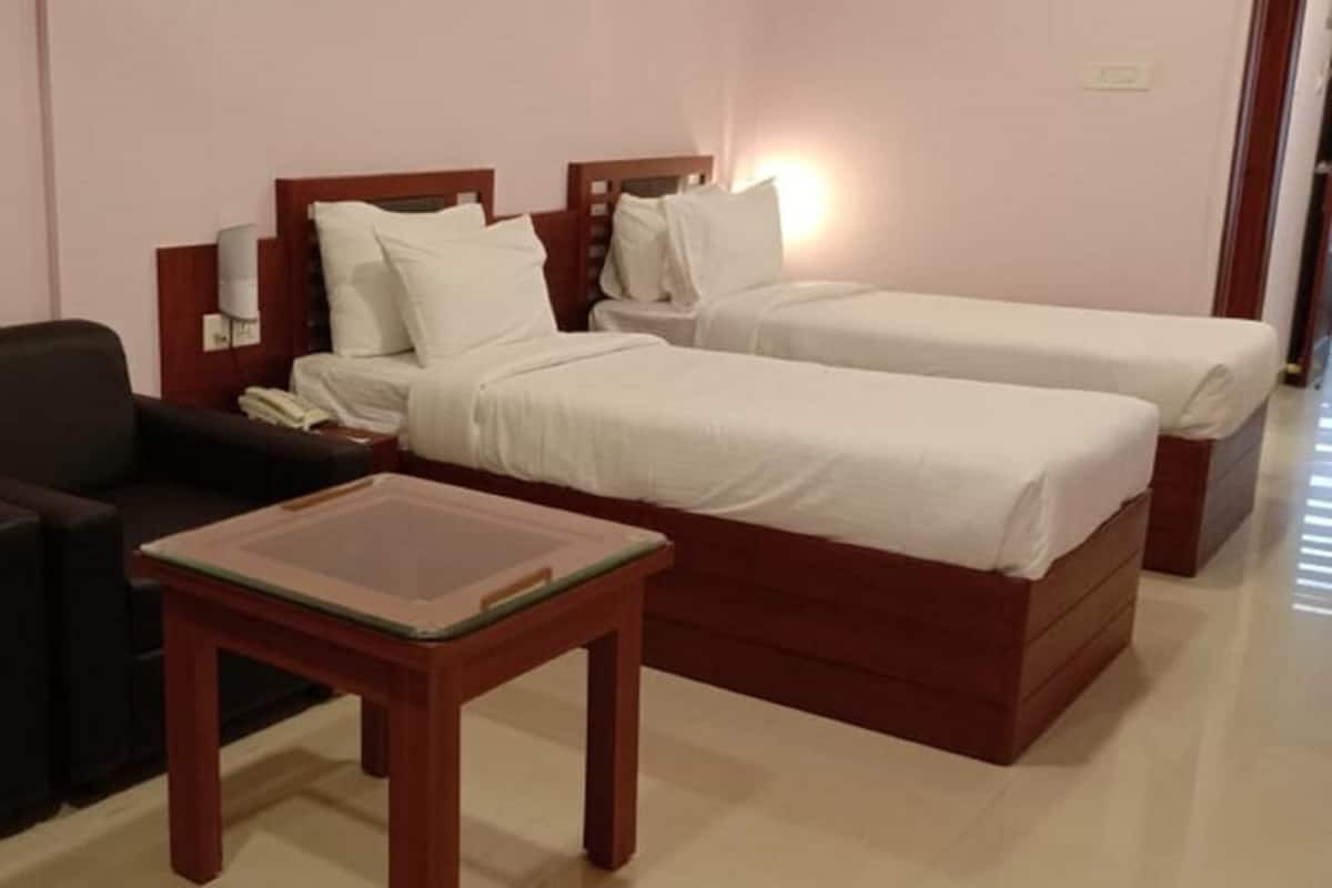 A hotel room with two beds, a small table, a chair, and a bedside table.