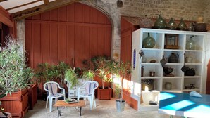 Una habitación rústica con una mesa y sillas de madera, plantas en macetas y una estantería con diversos objetos.