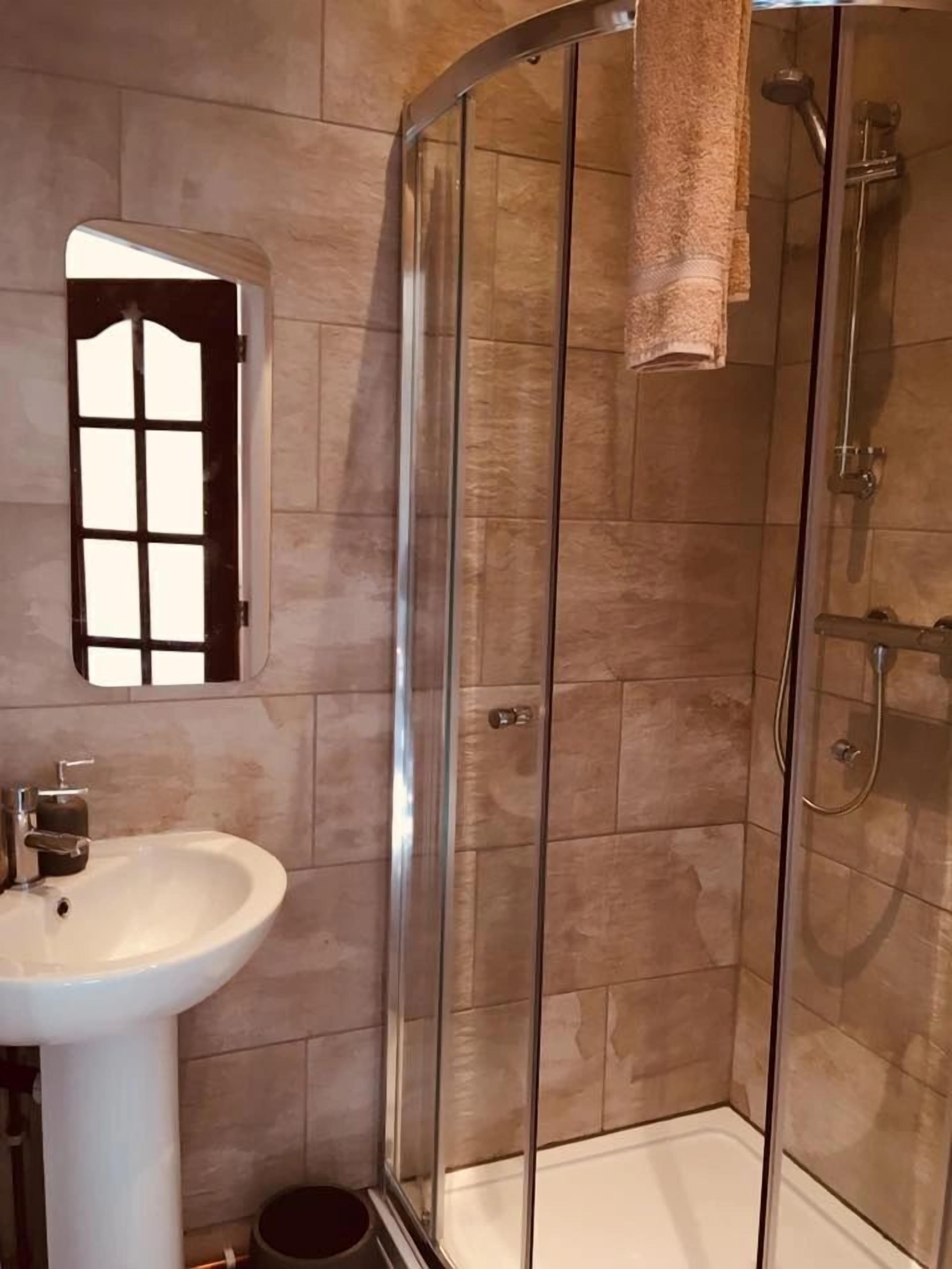 A corner bathroom with a glass-enclosed shower, a white sink, and a towel hanging on the wall.