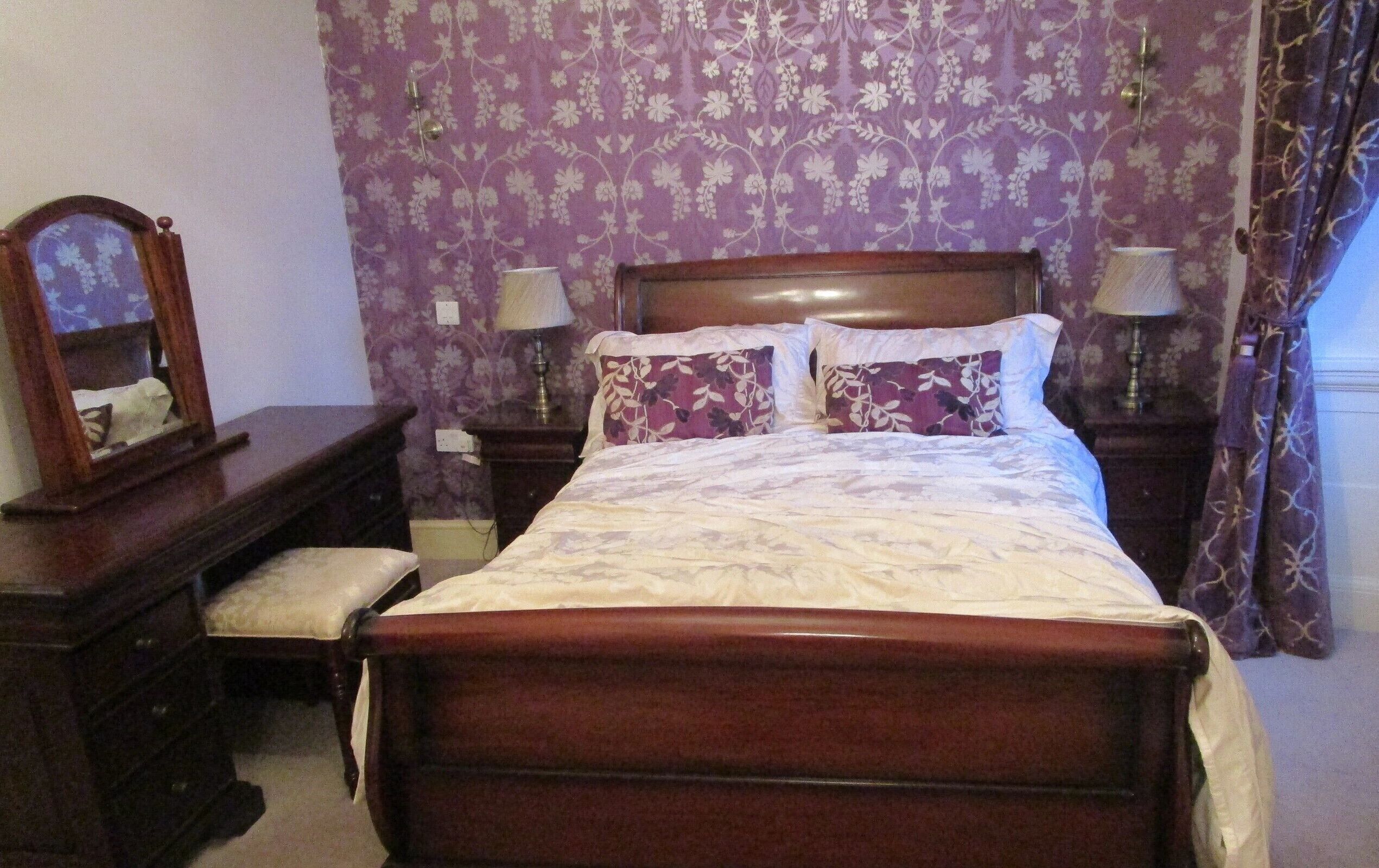 Un dormitorio con una cama de madera, dos mesitas de noche con lámparas, un tocador y un espejo.