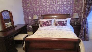 Un dormitorio con una cama de madera, dos mesitas de noche con lámparas, un tocador y un espejo.