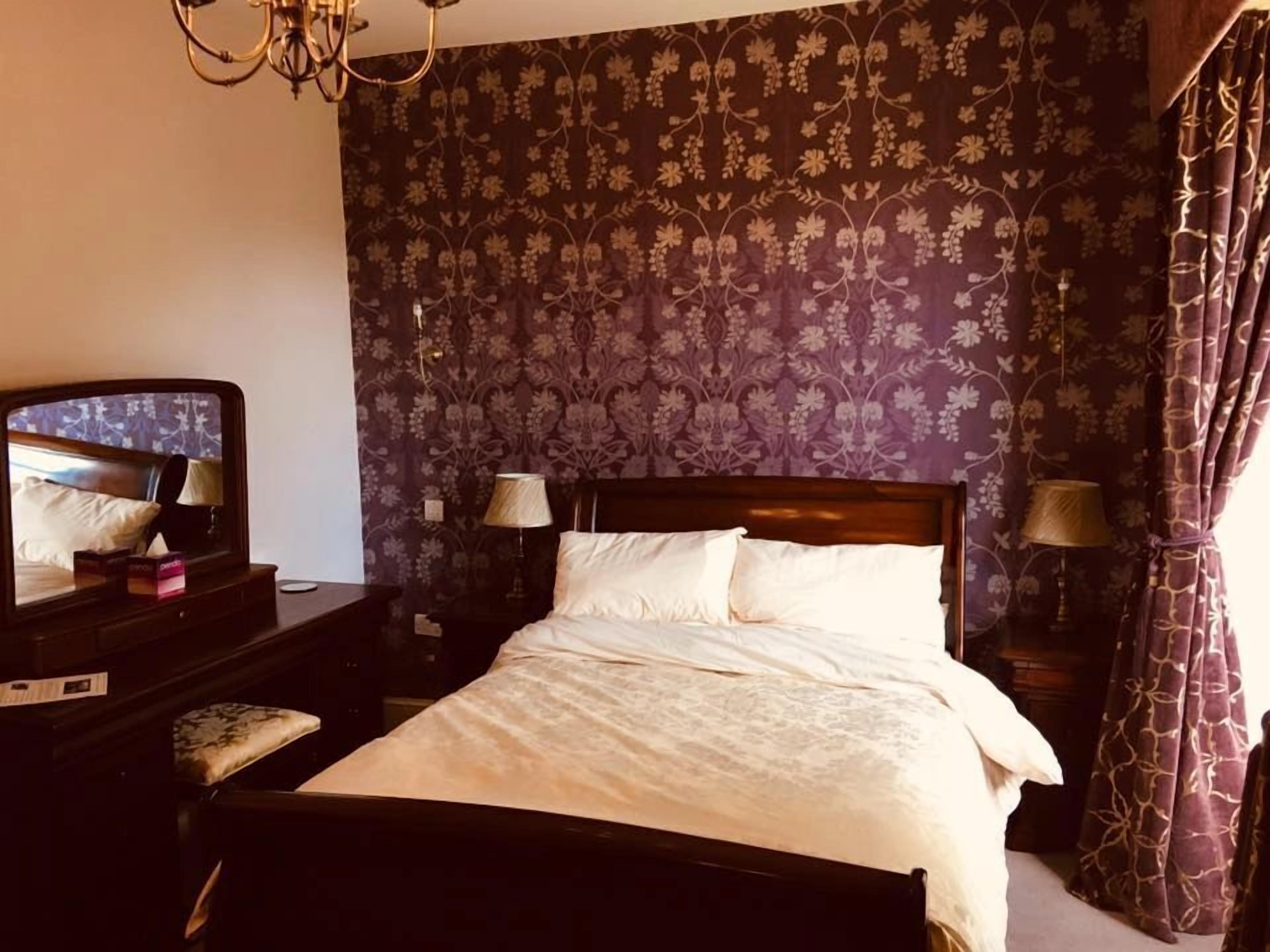 A hotel room with a bed, a nightstand, a lamp, a mirror, and a curtain.