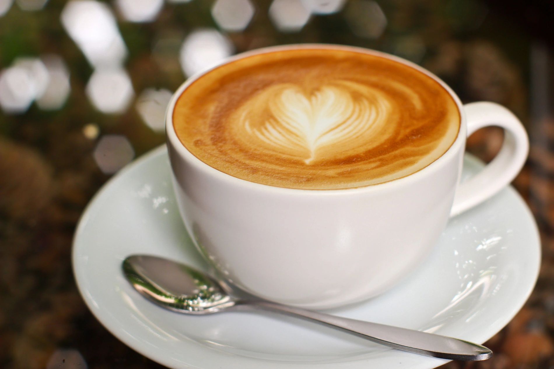 Una taza de café con arte de latte sobre un plato y cuchara.