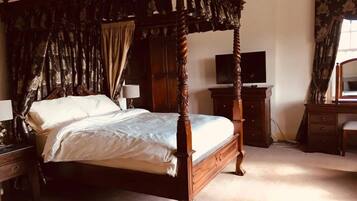 Una cama con dosel y cuatro columnas, con un televisor sobre un aparador, un escritorio y una silla en el dormitorio.