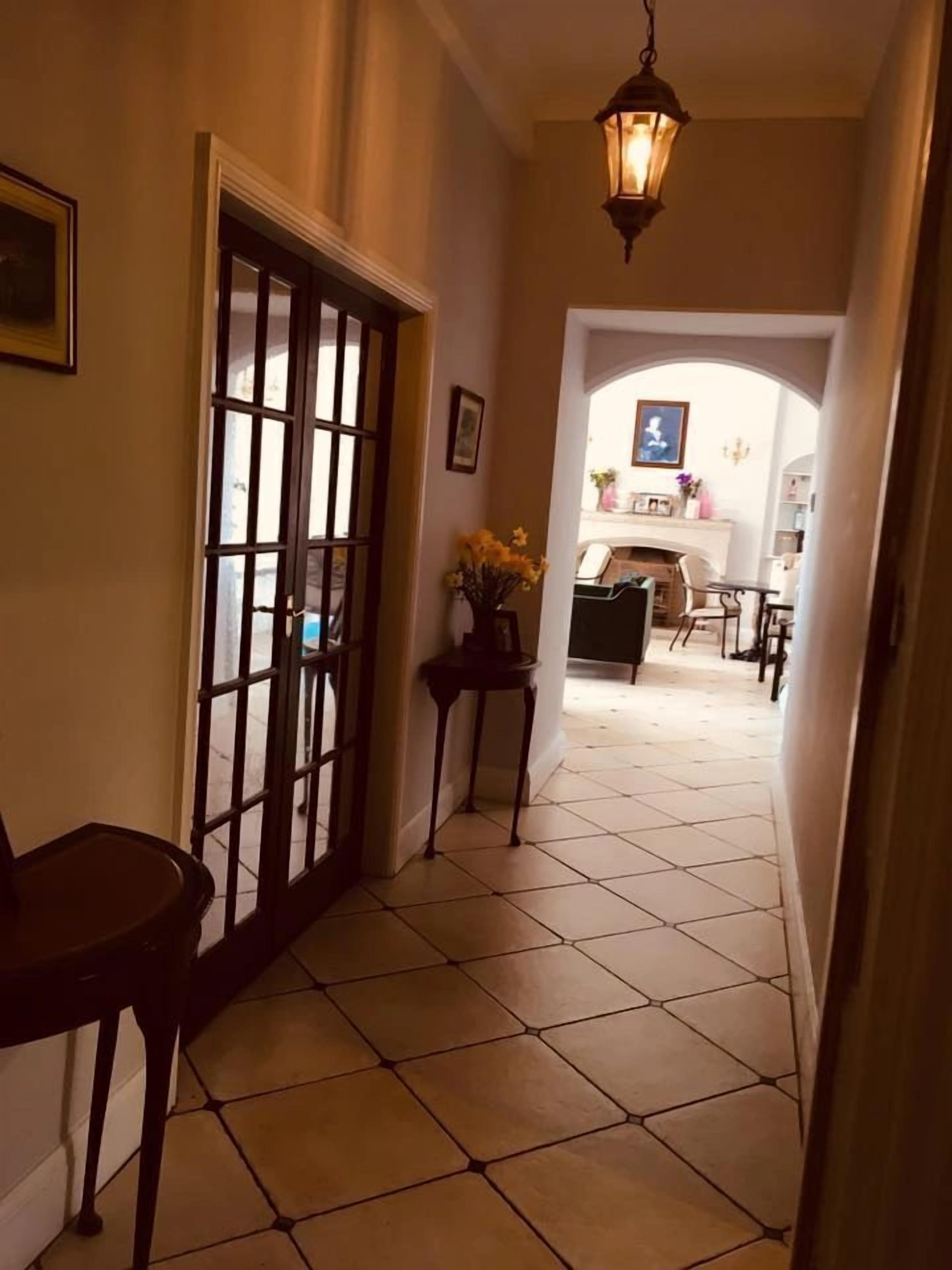 Un pasillo con suelo de baldosas, una puerta con panel de vidrio y una pequeña mesa con un jarrón de flores.