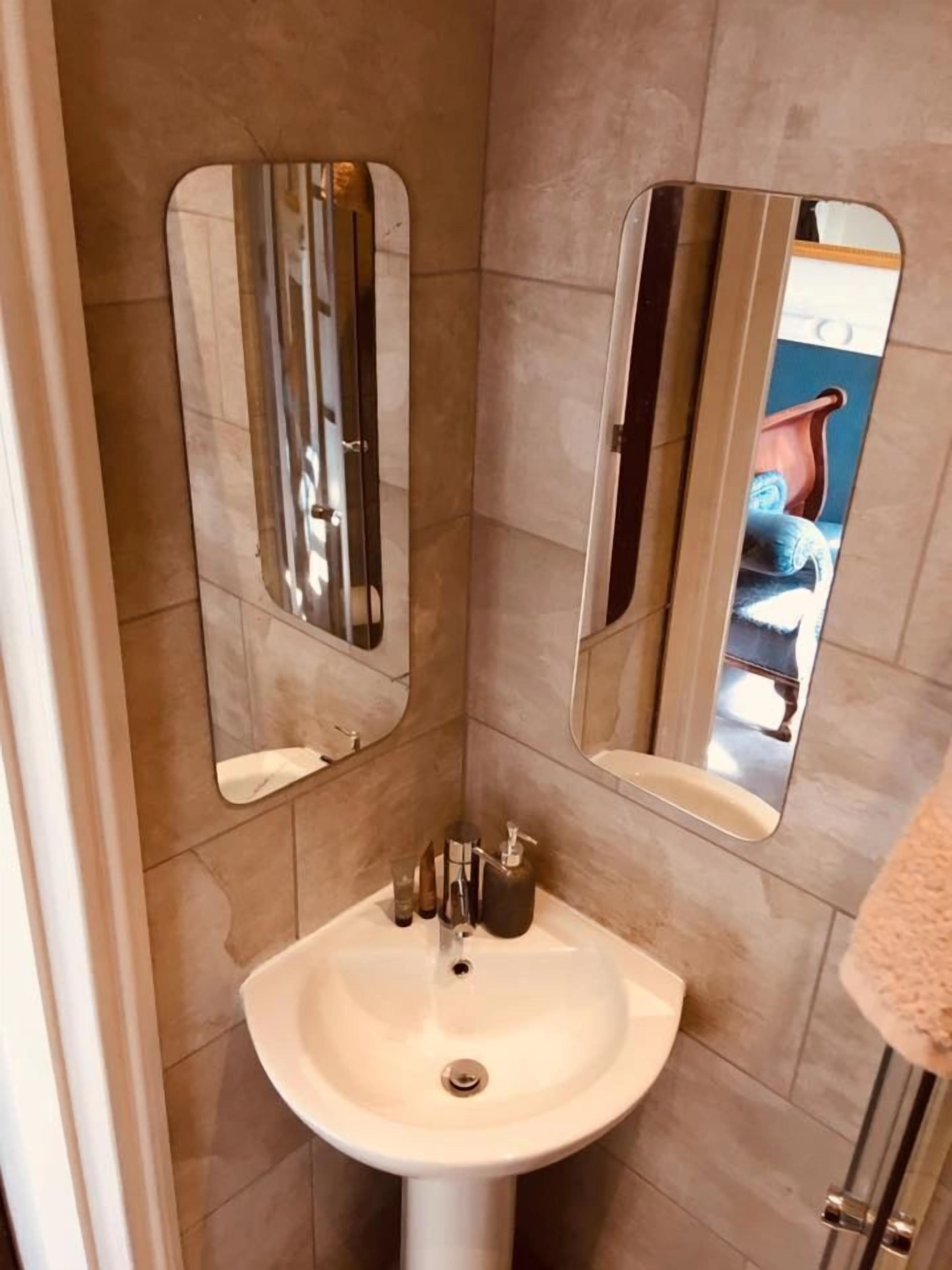 Een badkamer met een witte wastafel, twee spiegels en een handdoekrek.