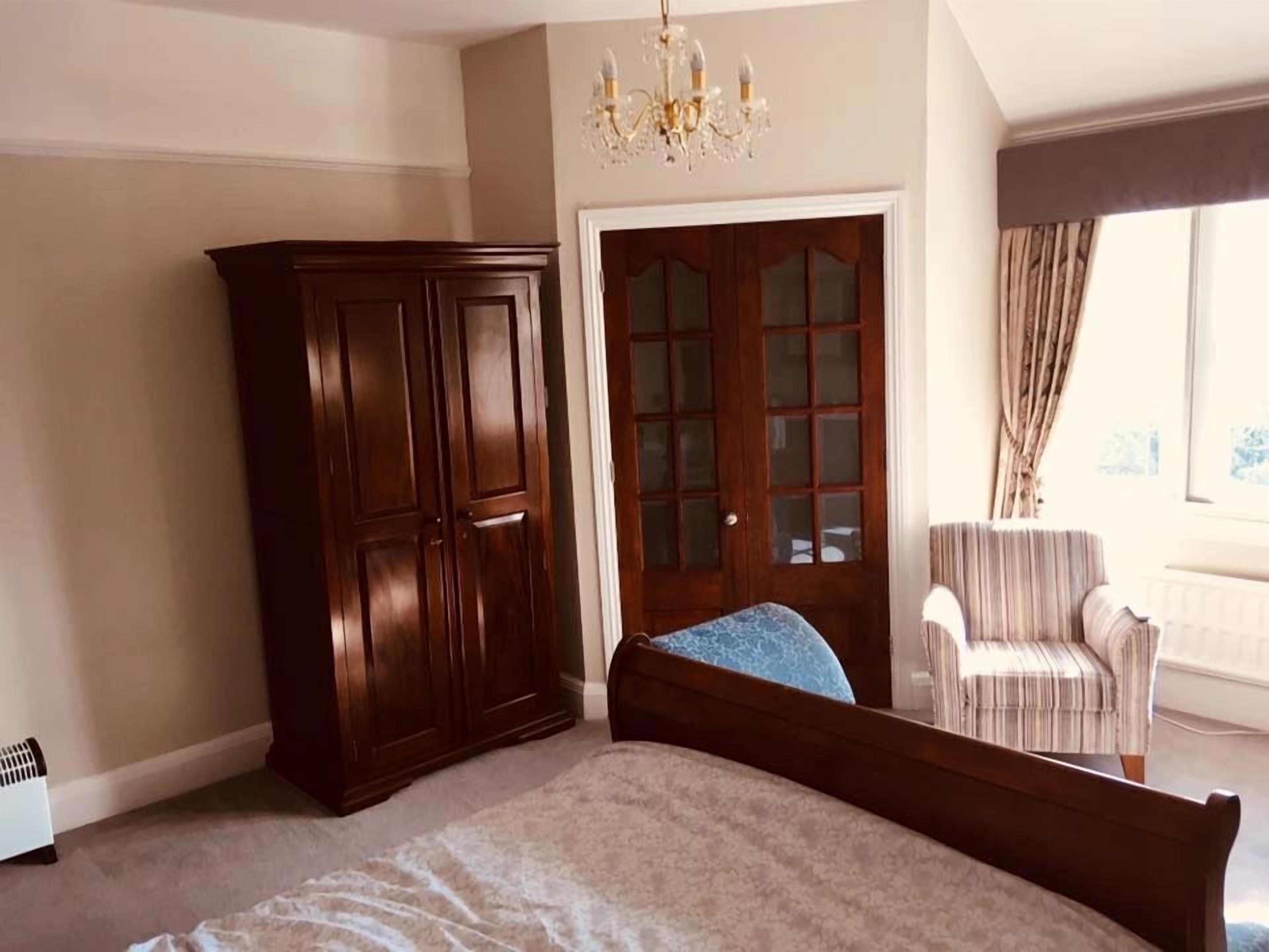 A bedroom with a large bed, a wardrobe, a chair, and a door with glass panels.
