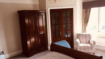 A bedroom with a large bed, a wardrobe, a chair, and a door with glass panels.