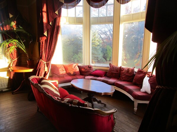 A cozy room with a curved red sofa, a small table, and a view of trees through large windows.
