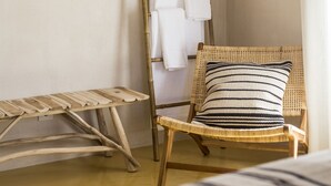 Een kamer met een houten ladder, een rieten stoel met een gestreept kussen en een bed met een gestreepte deken.