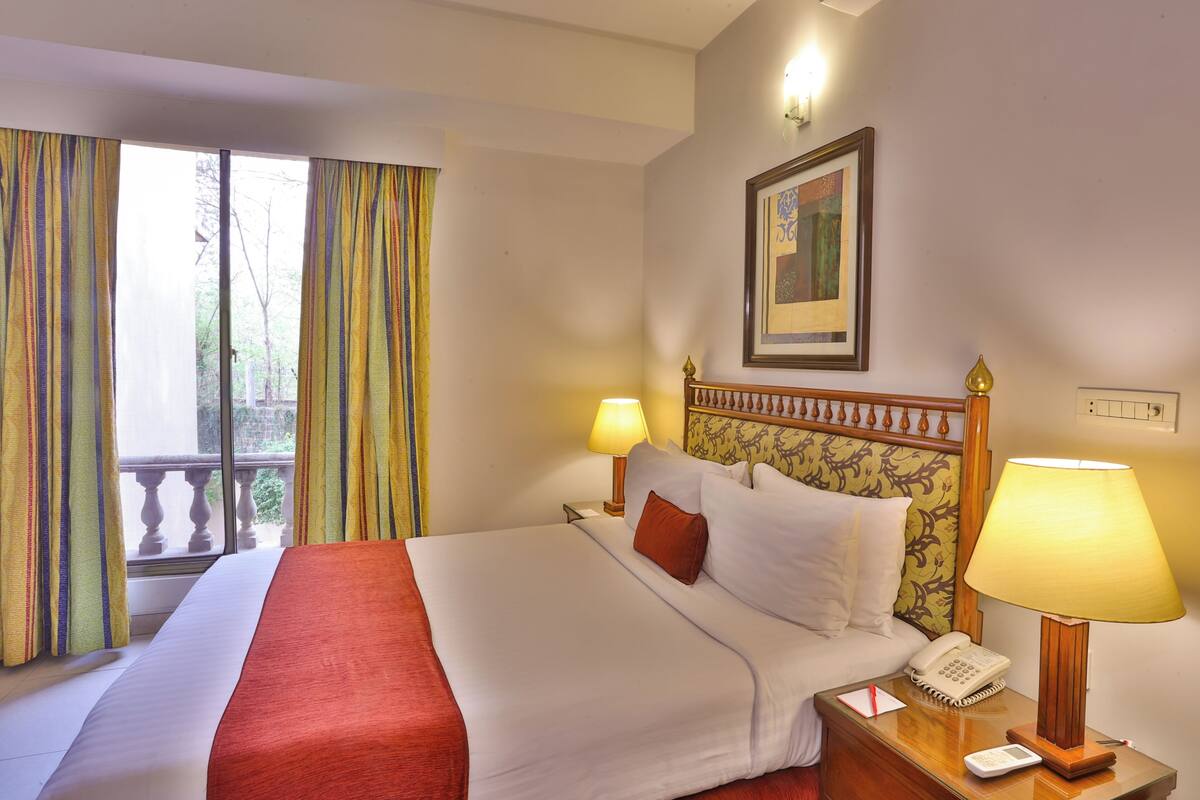 Une chambre d’hôtel avec un lit, deux lampes de chevet, un téléphone et une fenêtre avec des rideaux.