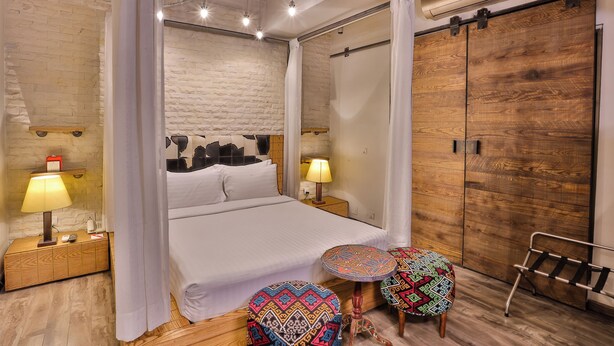 Une chambre à coucher avec un lit, des lampes de chevet, une armoire en bois, un banc et une petite table ronde.