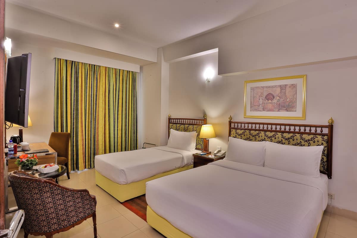 Une chambre d’hôtel avec deux lits, un bureau avec une chaise, une télévision et un rideau.