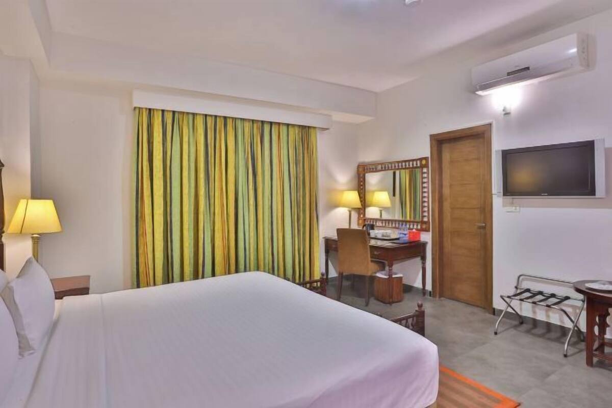 Habitación de hotel con cama, escritorio, silla, televisor y aire acondicionado.