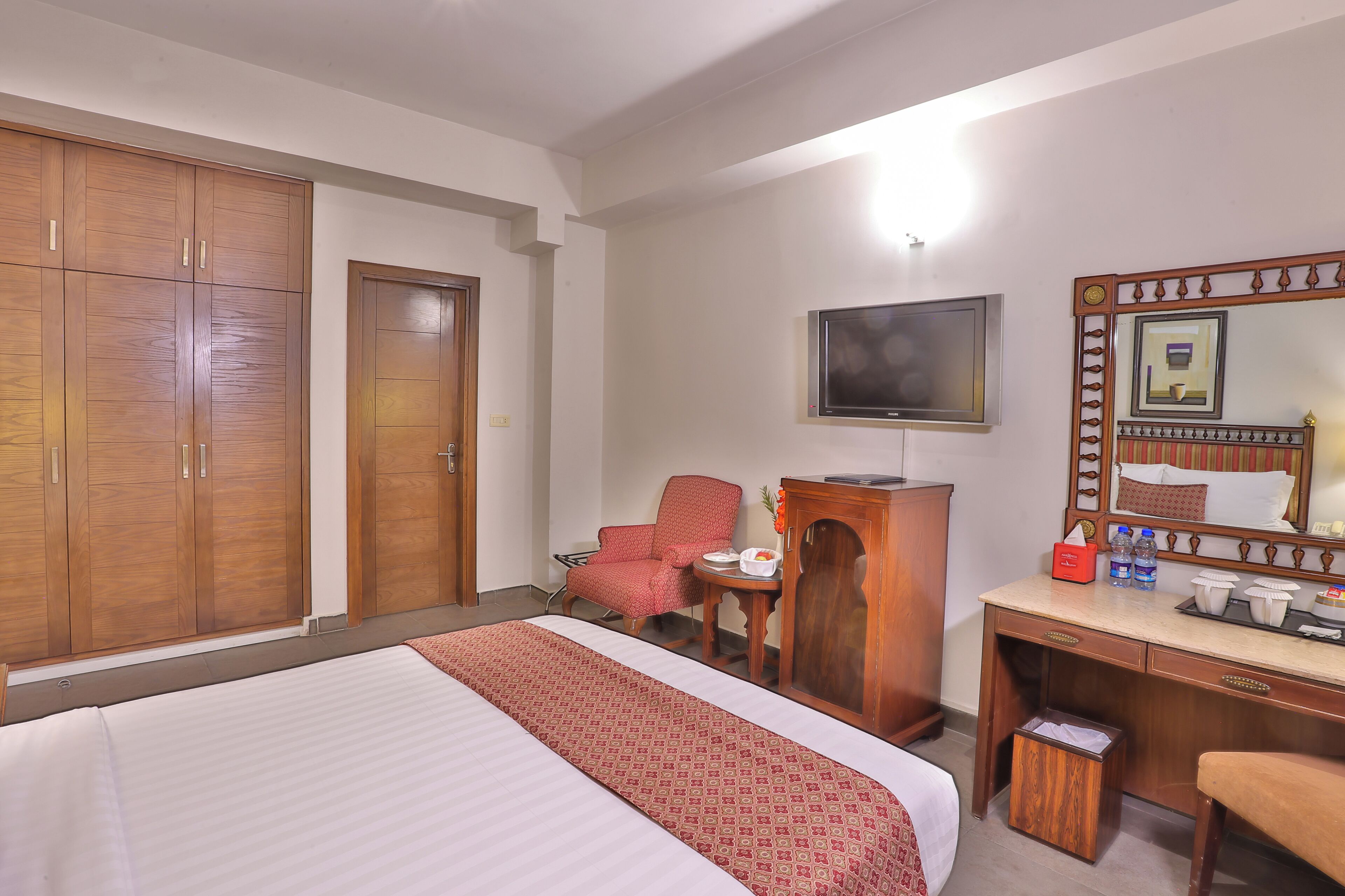 A hotel room with a bed, a desk, a chair, a wardrobe, a television, and a mirror.