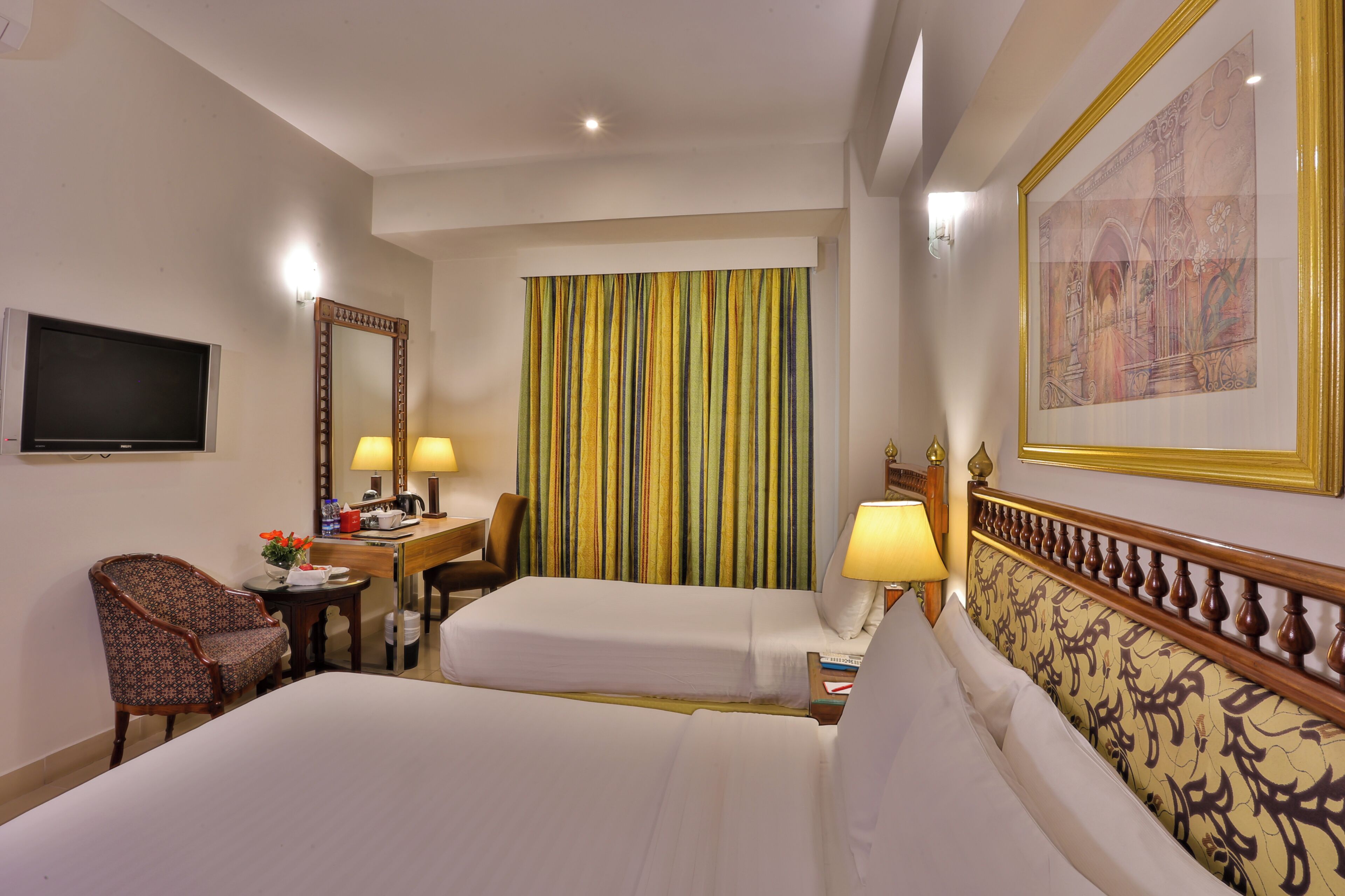 A hotel room with two beds, a desk, a chair, a TV, and a large window with curtains.