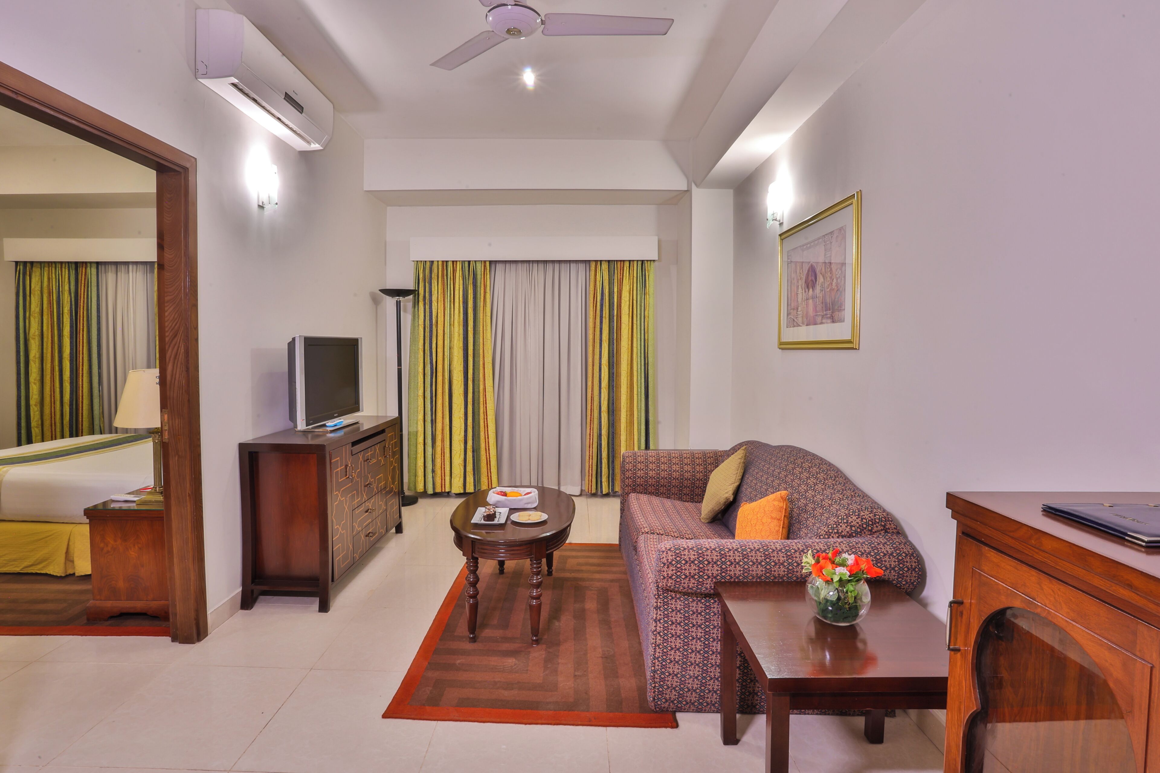 Habitación de hotel con cama, televisión, sofá, mesa de centro y escritorio con una computadora portátil.