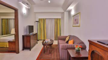 Habitación de hotel con cama, televisión, sofá, mesa de centro y escritorio con una computadora portátil.