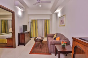 Habitación de hotel con cama, televisión, sofá, mesa de centro y escritorio con una computadora portátil.