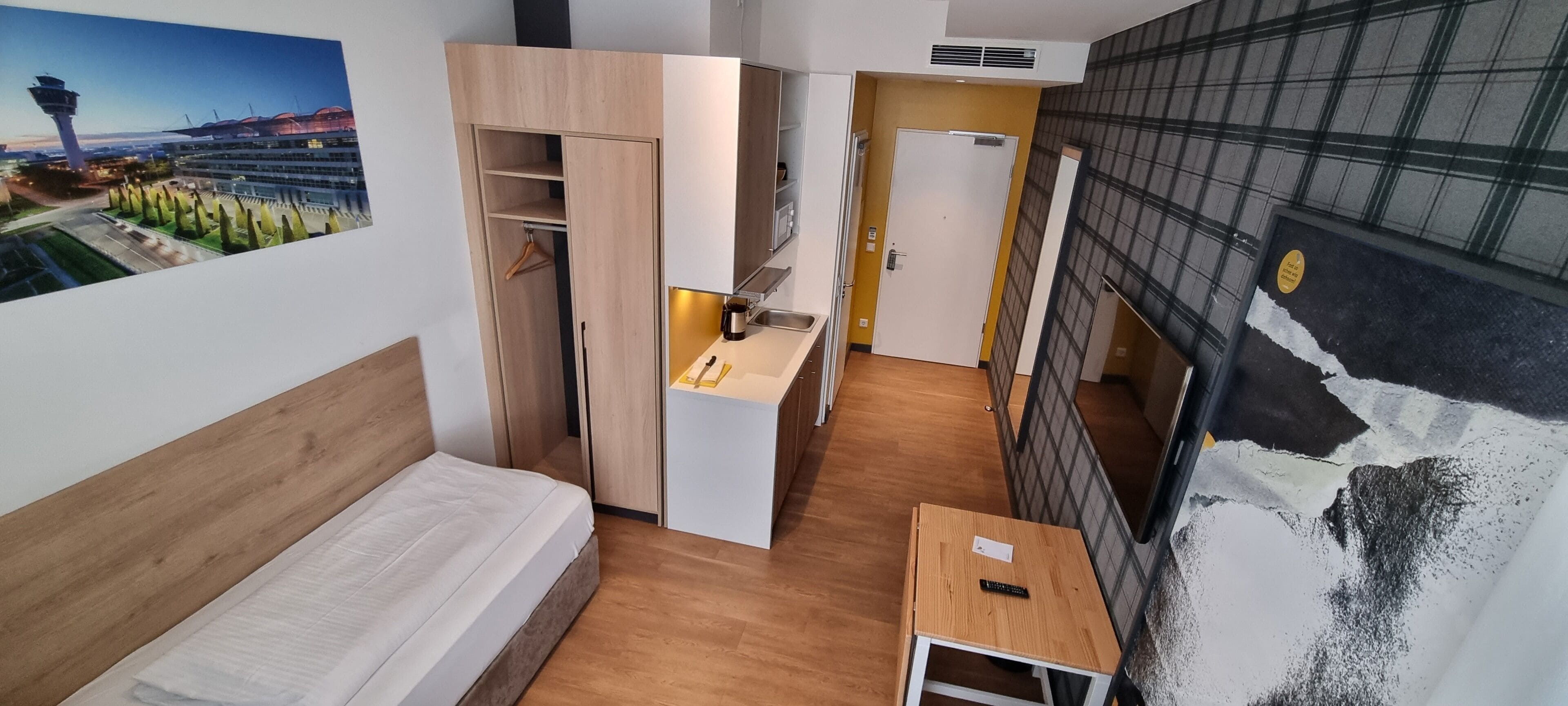 Habitación de hotel compacta con cama, una mesita, kitchenette y vistas a la ciudad.