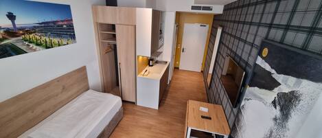 Habitación de hotel compacta con cama, una mesita, kitchenette y vistas a la ciudad.