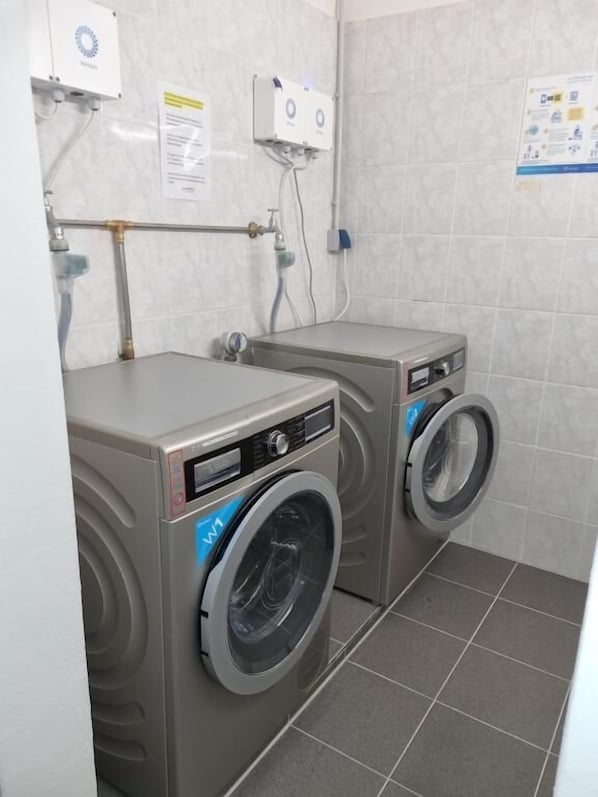 Un lavadero con dos lavadoras de carga frontal y un calentador de agua.