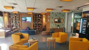 Recepció d'hotel amb butaques grogues, televisió, prestatge i màquina expenedora.