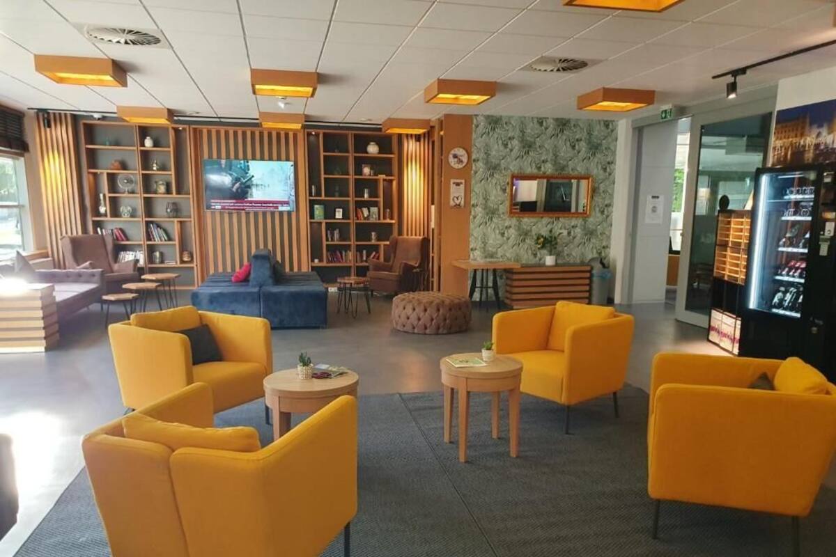 Una hall d'albergo con poltrone gialle, una televisione, una libreria e un distributore automatico.