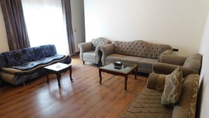 A living room with a dark blue sofa, a beige sofa, and a brown sofa. There are two wooden coffee tables and a small table with a box and remote. - Sunset Destination (Islamabad)