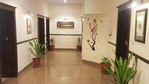 A hallway with potted plants, framed pictures on the walls, and a tiled floor. - Sunset Destination (Islamabad)
