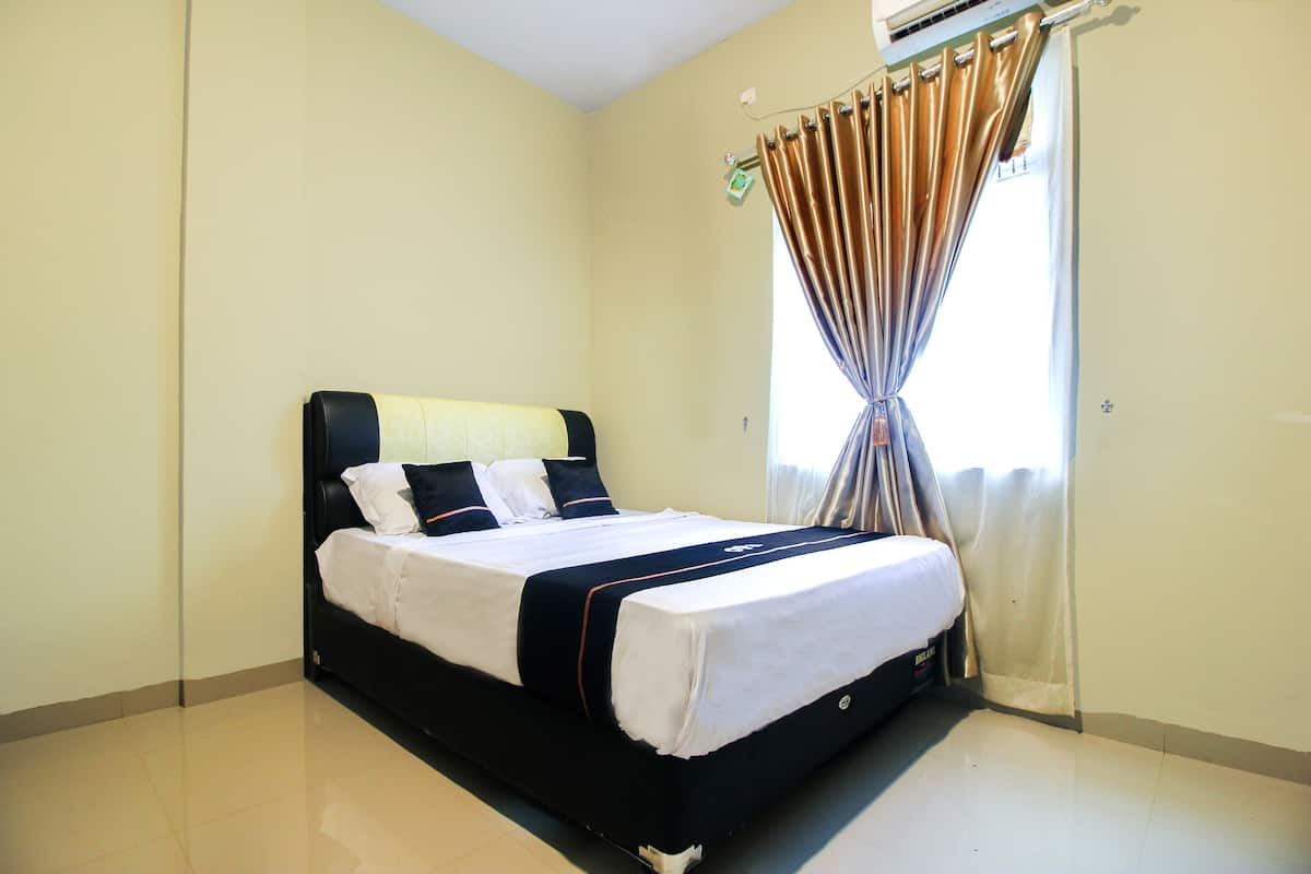 A neatly made bed with a black headboard and white bedding, a window with curtains, and a wall-mounted air conditioning unit.