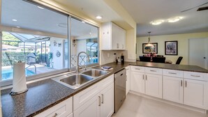 Una cocina moderna con armarios blancos, electrodomésticos de acero inoxidable y un amplio ventanal con vista a una zona de piscina.