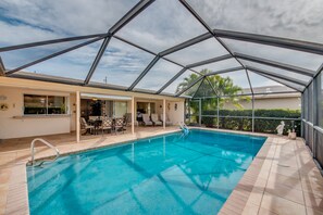 Una piscina interna con tetto in vetro, una terrazza solarium con sedie e vista su palme.